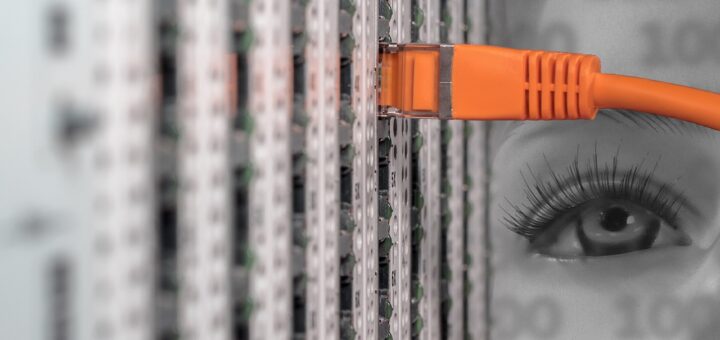 serwer z pomarańczowym kablem LAN wpiętym w gniazdo. W tle widać pół twarzy kobiety pokryte cieniem zer i jedynek